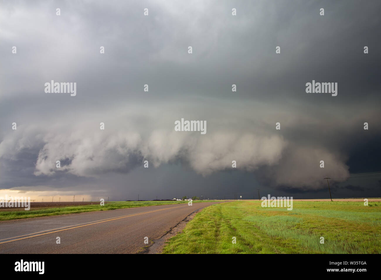 A big supercell storm with a shelf cloud and a wall cloud looms over a road in the rural countryside. Stock Photo