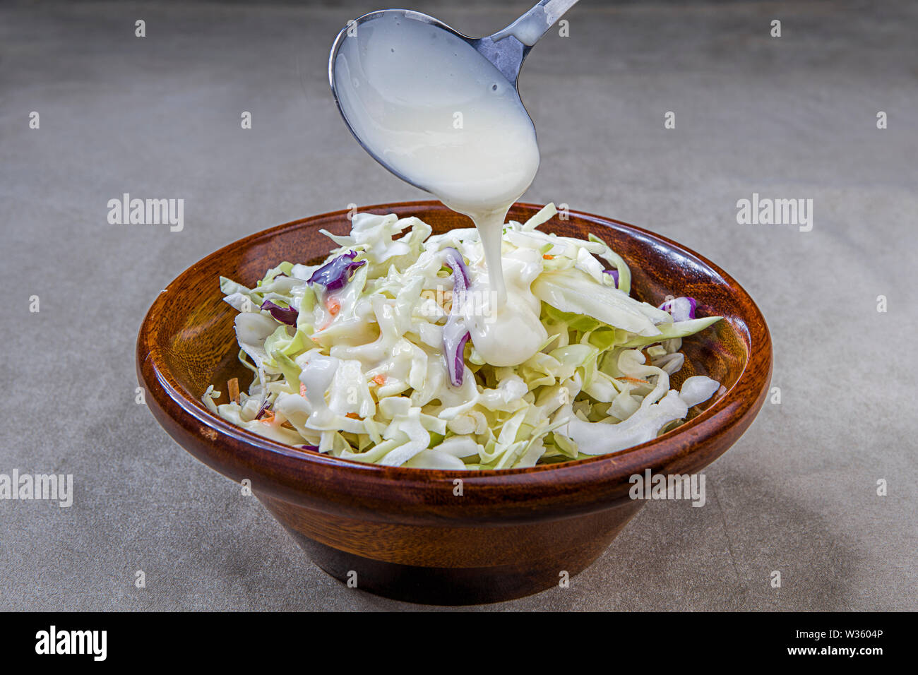 A close up photo of pouring coleslaw dressing over a bowl of raw