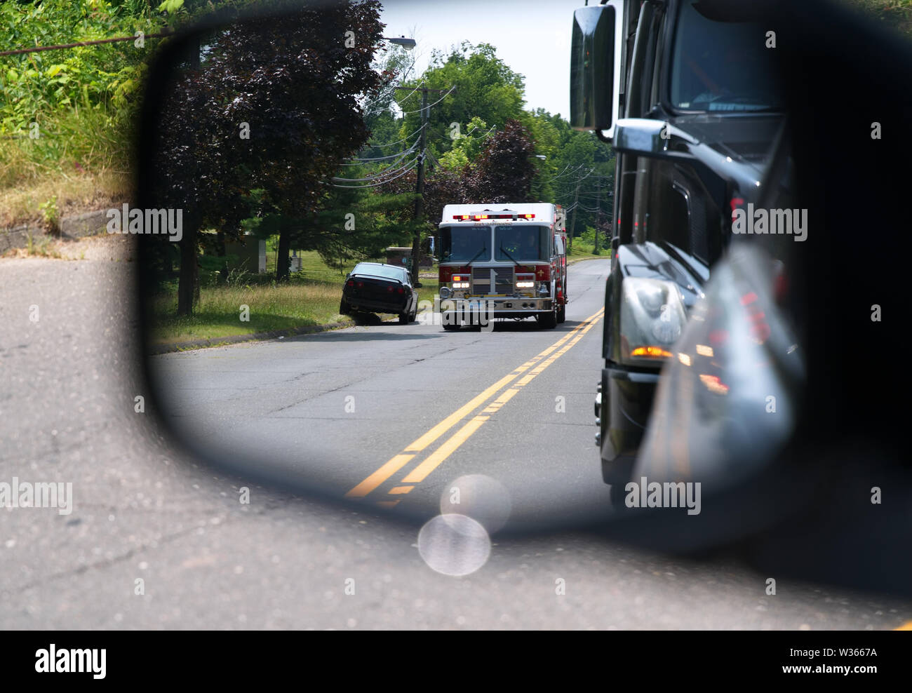 Middletown, CT USA. Car side mirror view of vehicles pulling over for a fast fire truck responding to an emergency. Stock Photo