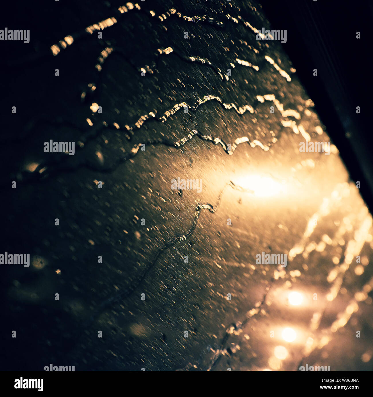 Beautiful background with rain drop on window, traffic light with close up shoot of car glass at night make bokeh in cyan and yellow color Stock Photo