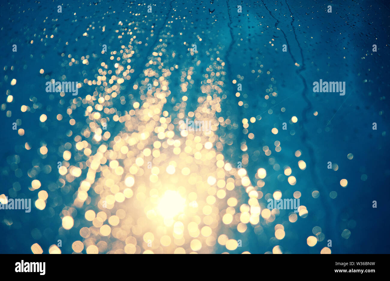 Beautiful background with rain drop on window, traffic light with close up shoot of car glass at night make bokeh in cyan and yellow color Stock Photo