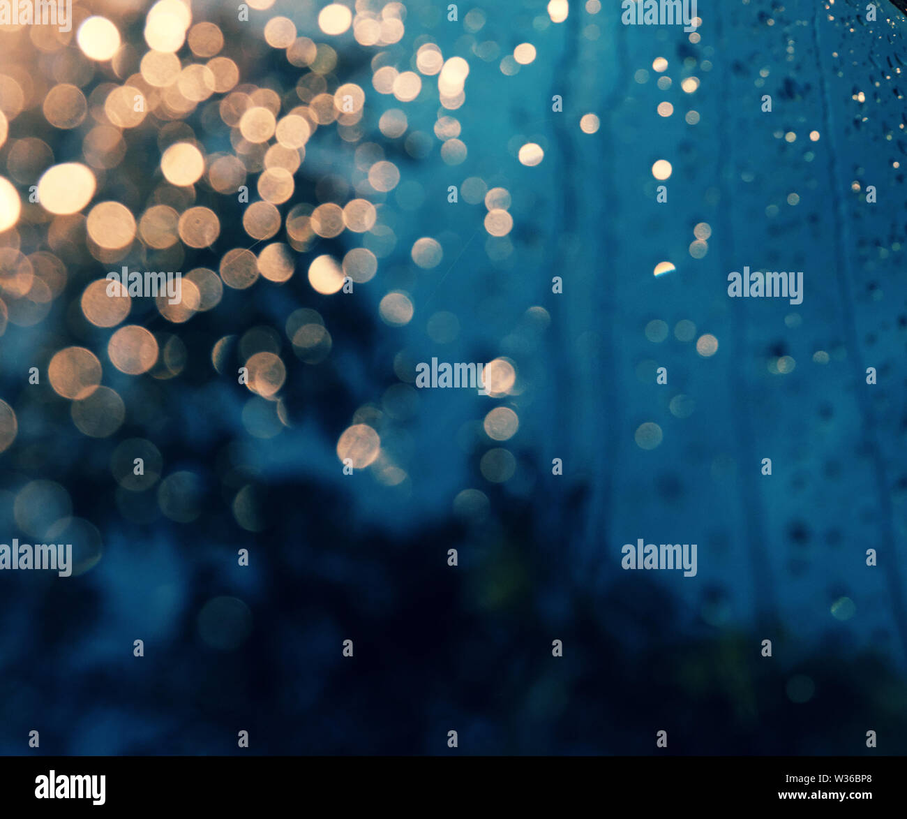 Beautiful background with rain drop on window, traffic light with close up shoot of car glass at night make bokeh in cyan and yellow color Stock Photo