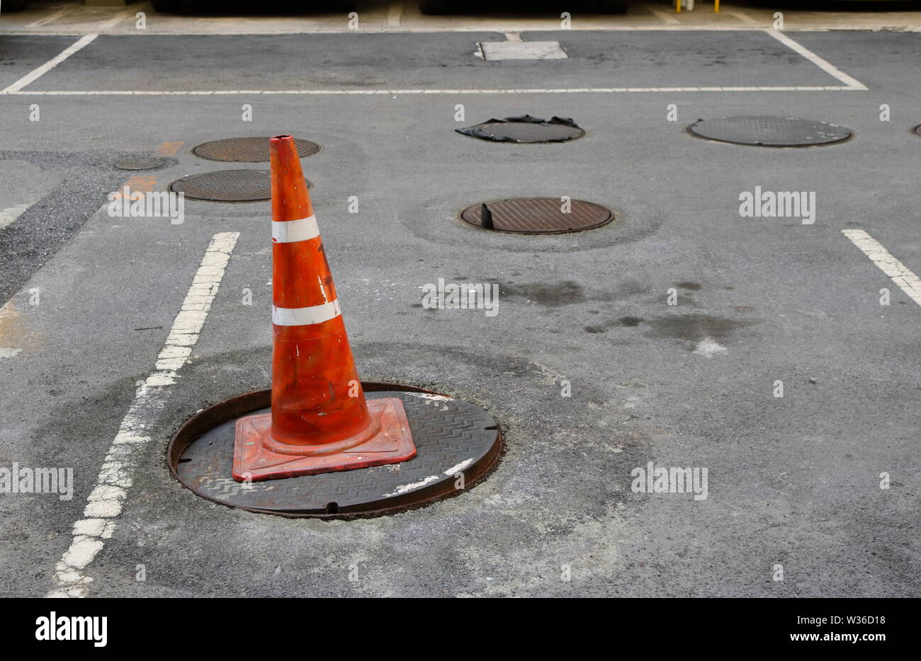 Closeup of old traffic cone on damaged drain cover, safety concept Stock Photo