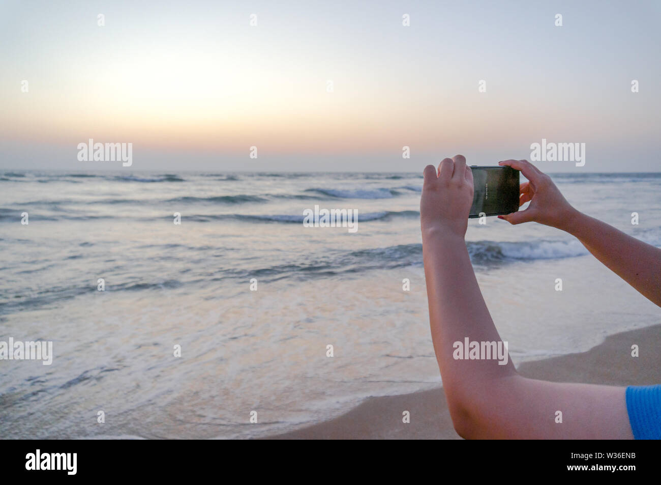 Hands of young indian woman holding up a phone to click a picture of a beautiful beach in gujarat Stock Photo