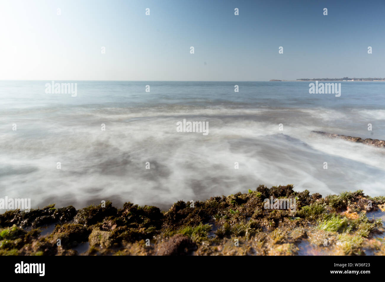 Long exposure of rocky beach with blurred waves and moss covered rocks Stock Photo