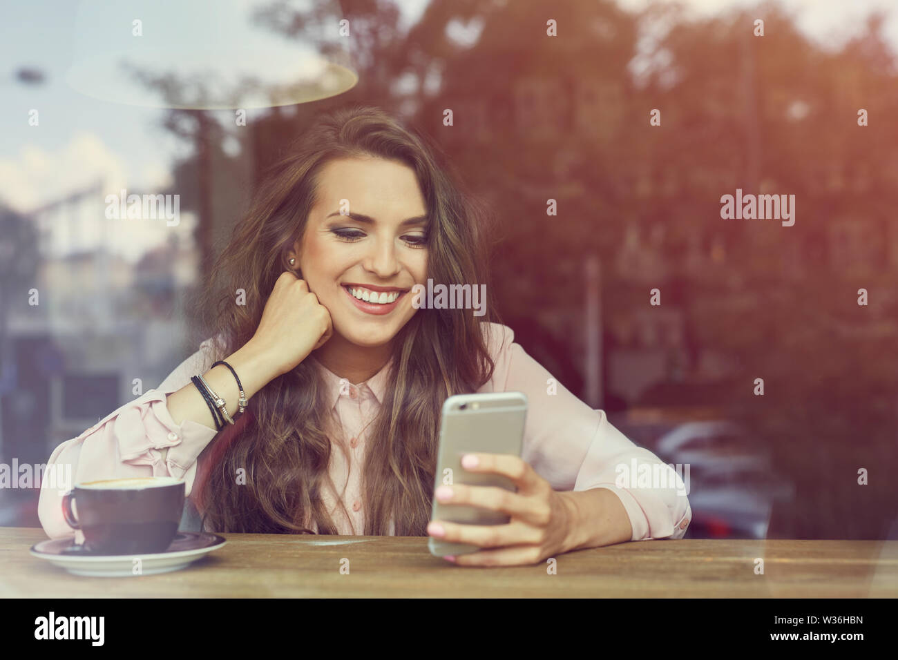 Happy young woman sitting in coffee shop texting on her smart phone ...