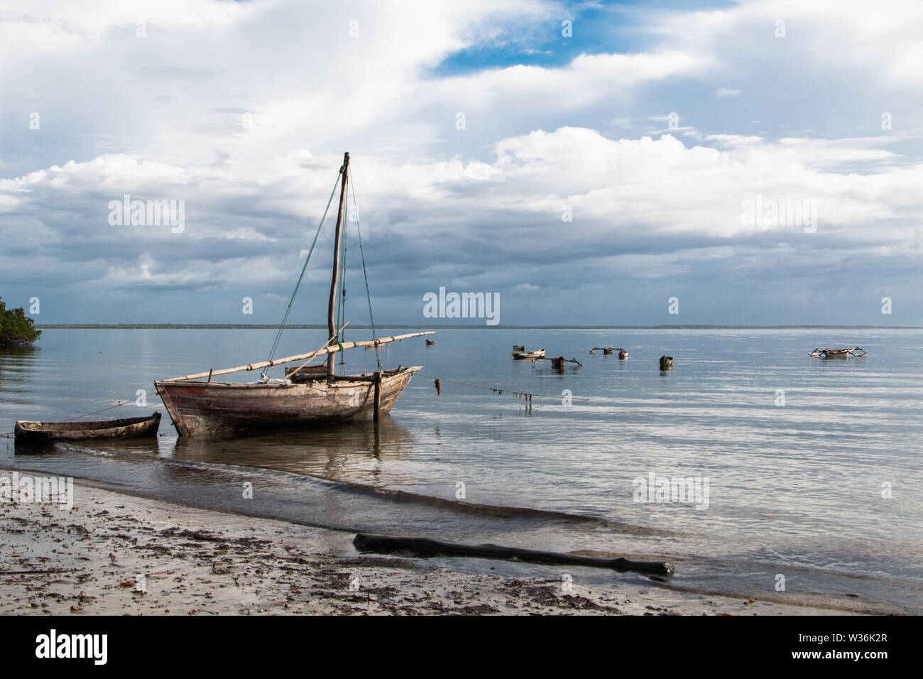 Small wooden sailboats on the water at the beach at sunrise in Mafia Island, Tanzania, with cloudy sky and calm water with surrounding dugout canoes. Stock Photo