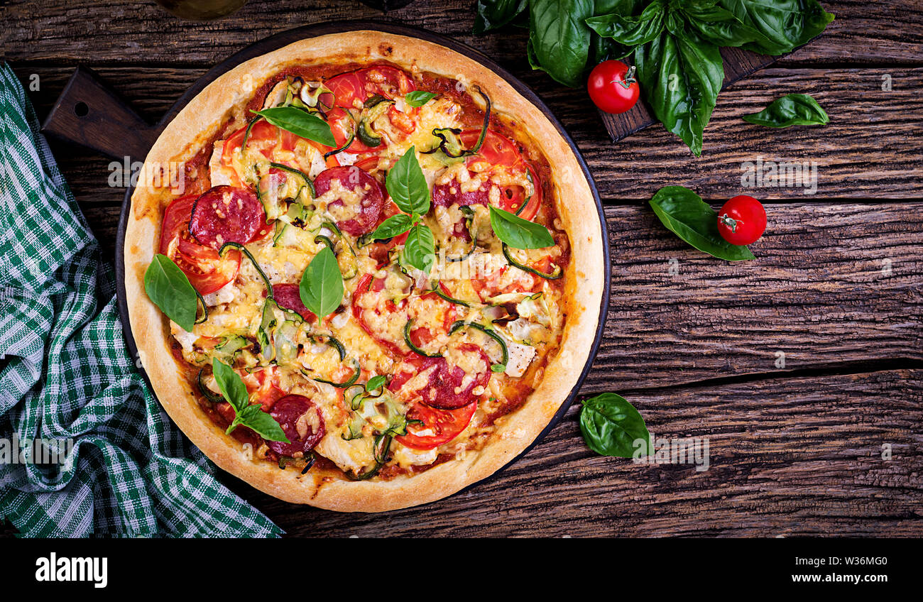 Italian pizza with chicken, salami, zucchini, tomatoes and herbs on