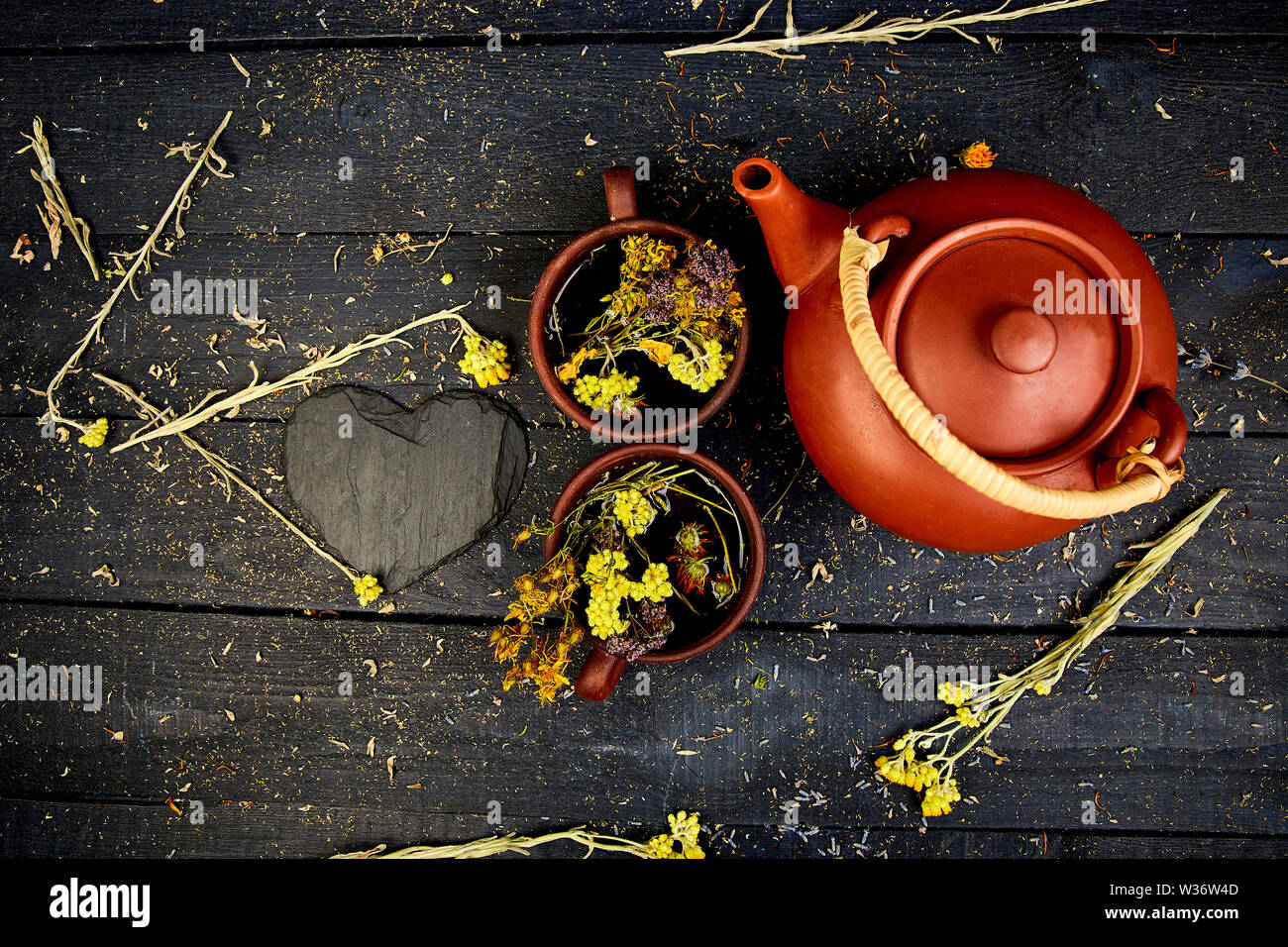 Two Cup of herbal tea - tutsan, sagebrush, oregano, helichrysum, lavender near brown teapot on dark wooden background. Herbal tea. Dry Herbs and flowe Stock Photo