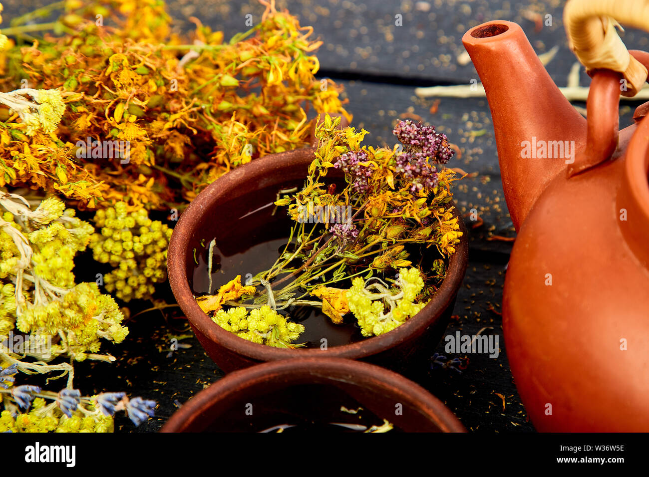 Cup of herbal tea - tutsan, sagebrush, oregano, helichrysum, lavender near brown teapot on dark wooden background. Herbal tea. Dry Herbs and flowers, Stock Photo