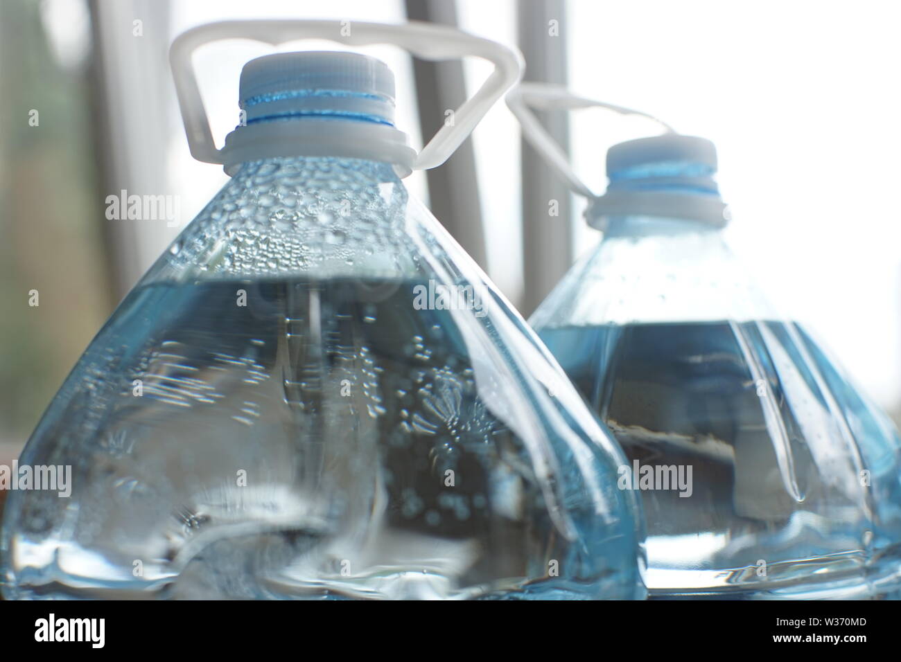 Two five-liter plastic bottles full of water, close-up of the top with lids and handles, condensation with drops inside the bottle Stock Photo