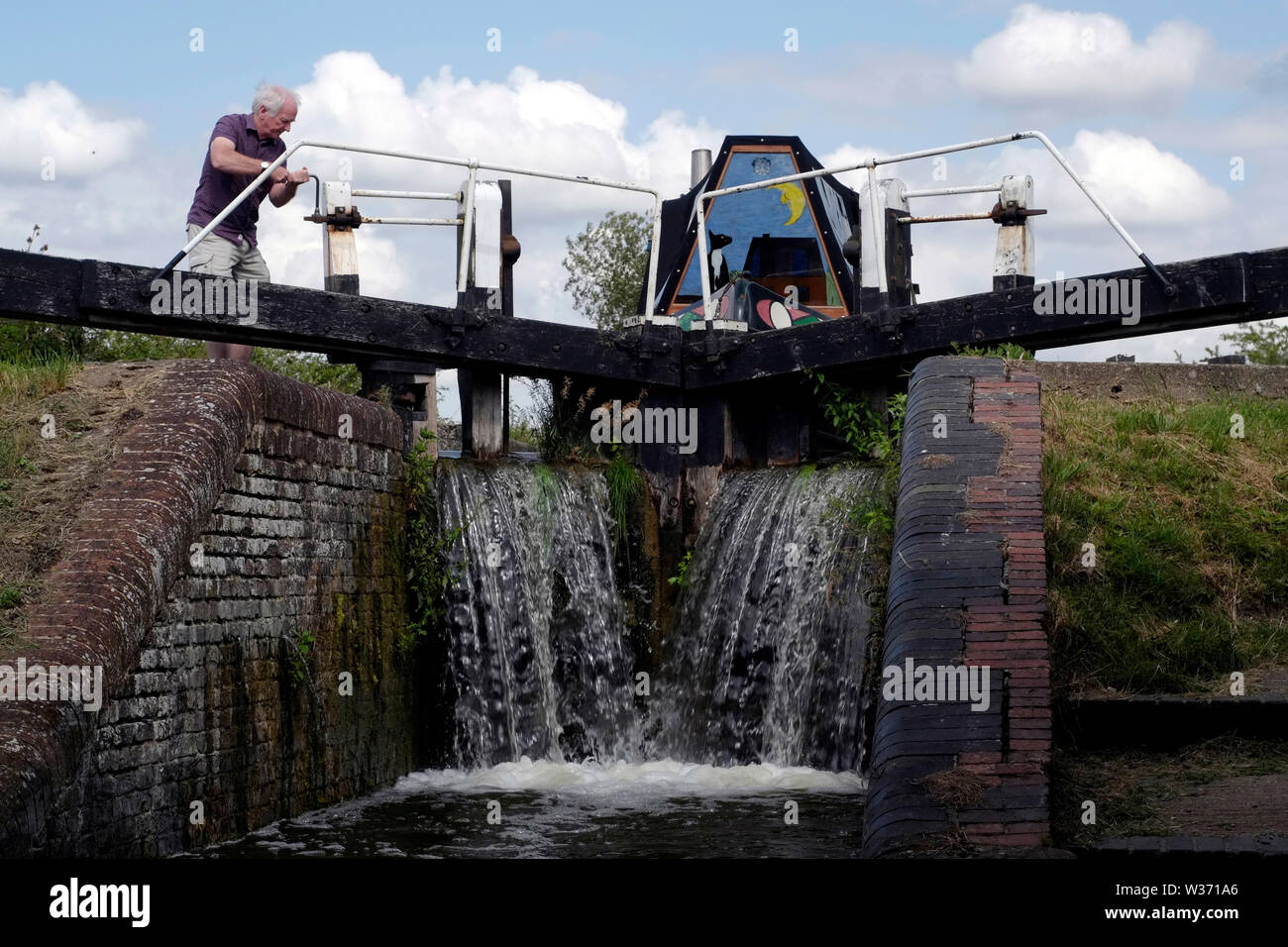 A man Cranking canal lock gates to release water level and lower his canal boat on the Grand Union Canal near Aylesbury, Buckinghamshire. Stock Photo