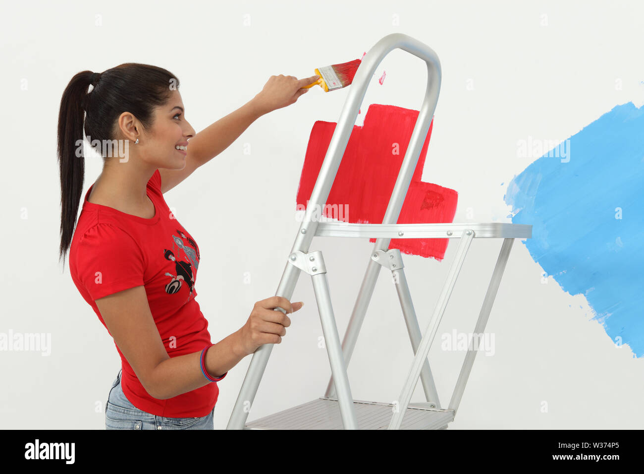 Indian young woman painting a wall and smiling Stock Photo - Alamy