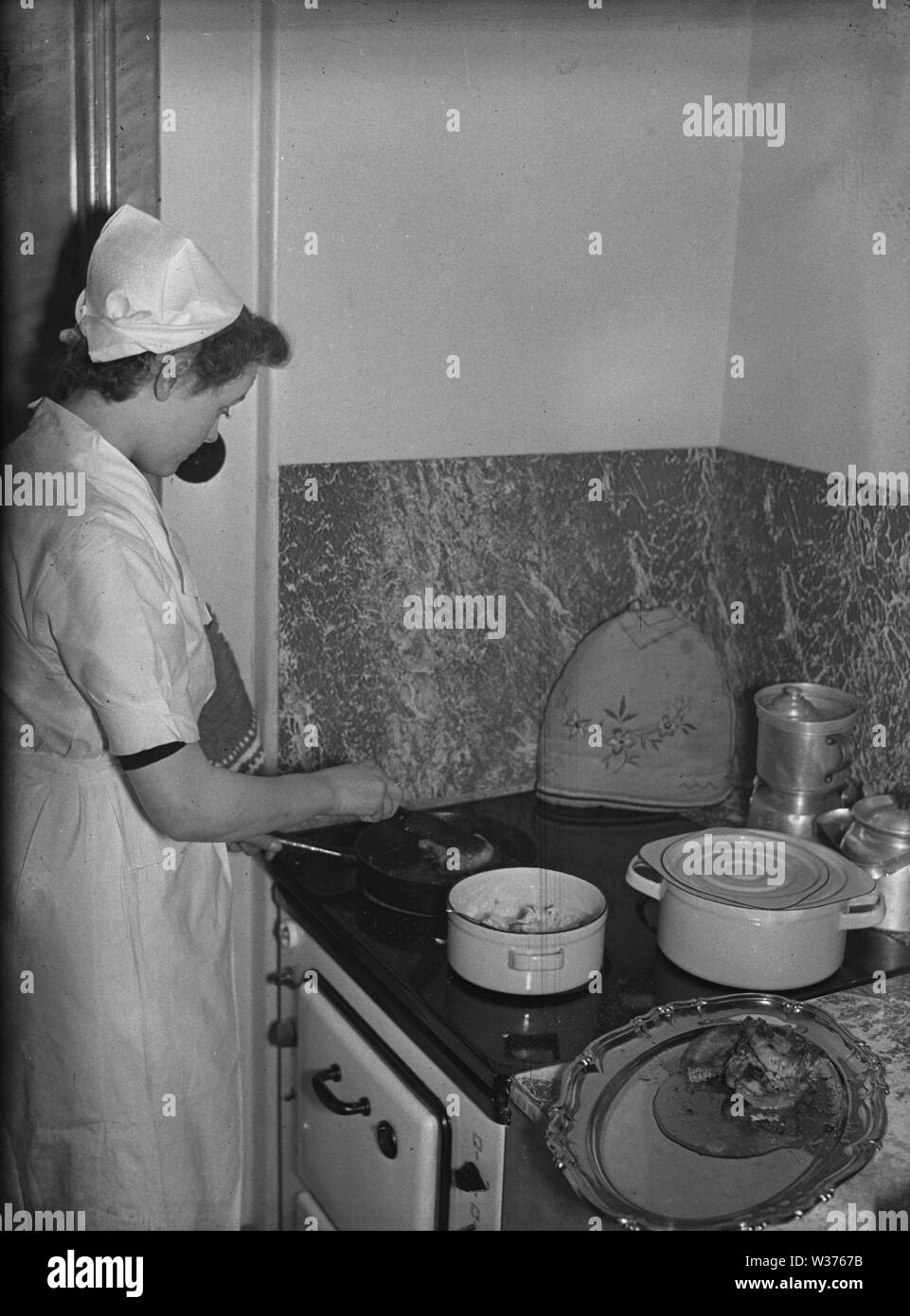 Cooking in the 1940s. A young woman employed as a house maid is cooking a meal on the kitchen stove. Sweden 1940. Kristoffersson ref 55-5 Stock Photo