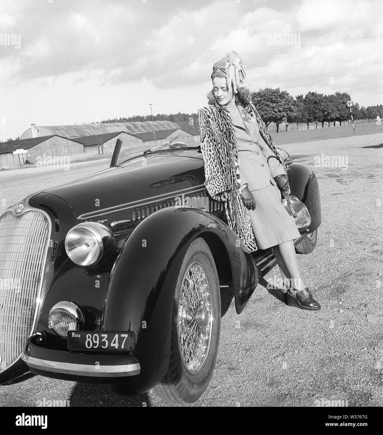 Women's fashion in the 1940s. A young woman in a typical 1940s outfit. A matching skirt and jacket with a leopard patterened coat hanging over her shoulders. The car is a italian sports car from the car manufacturer Alfa Romeo.   Sweden 1946. Kristoffersson Ref X1-5 Stock Photo
