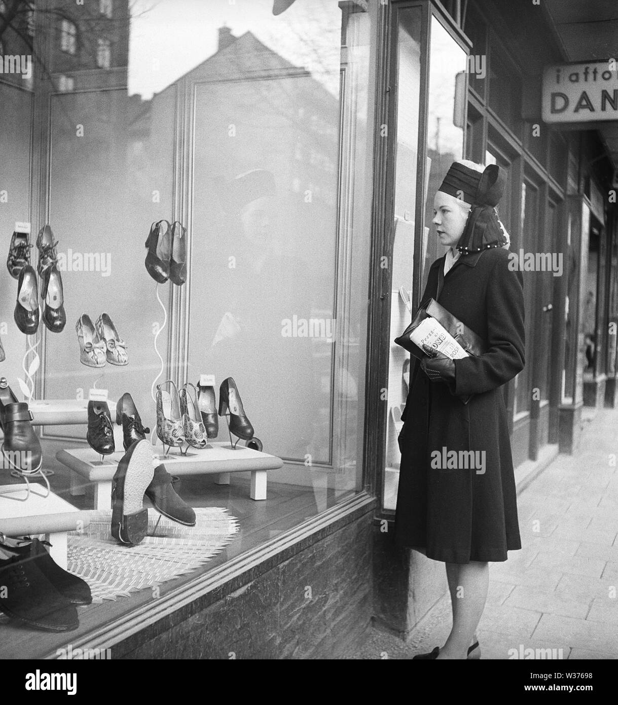 Window shopping in the 1940s. A woman is standing outside a boutique displaying the latest fashion in women's shoes. She is wearing a dark coat and a matching fashionable hat. Sweden 1946. Kristoffersson AB21-12 Stock Photo