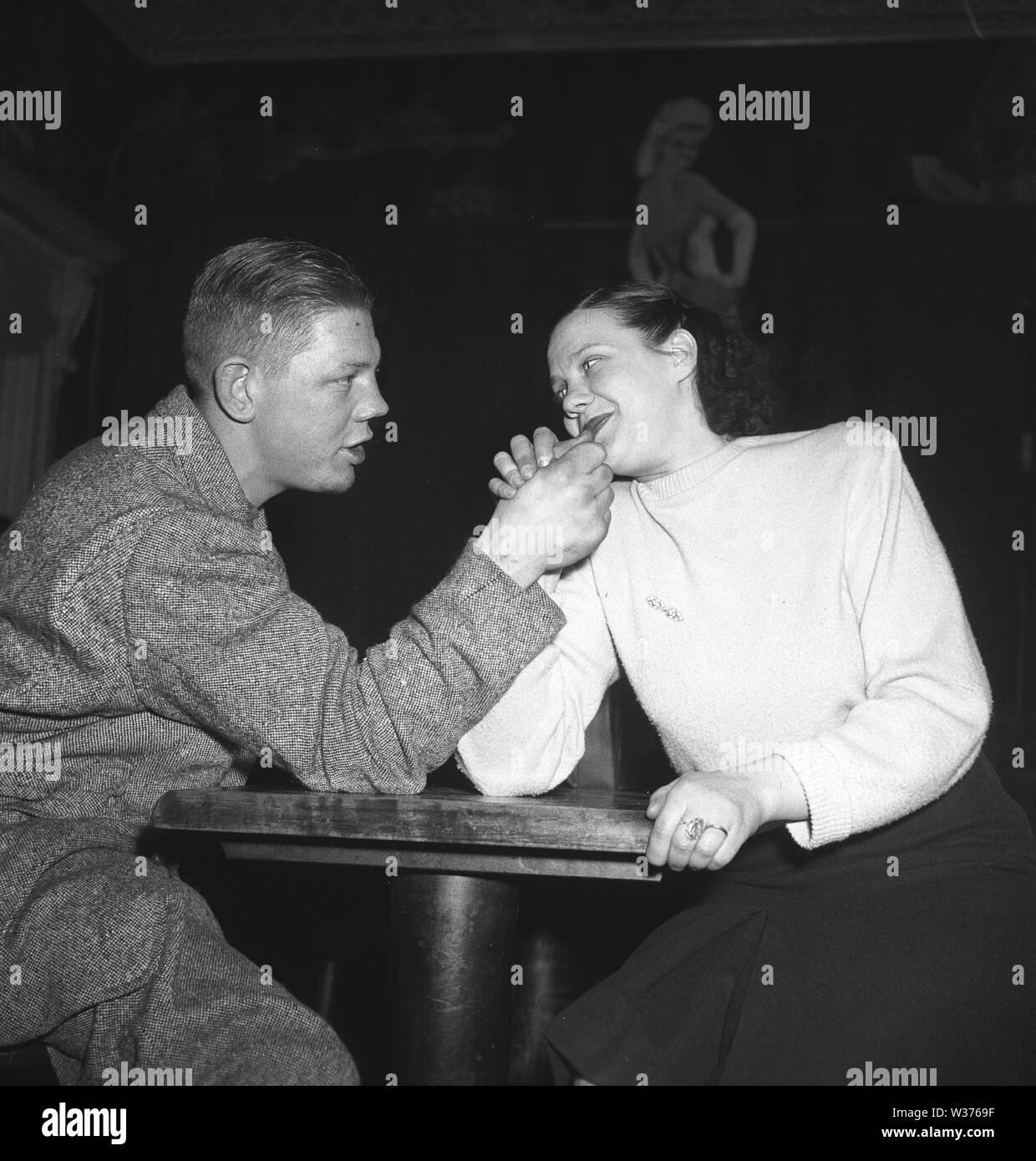 Who's the strongest? A young couple try their strenght at armwrestling in a restaurant. Sweden 1948 Kristoffersson Ref AH21-7 Stock Photo