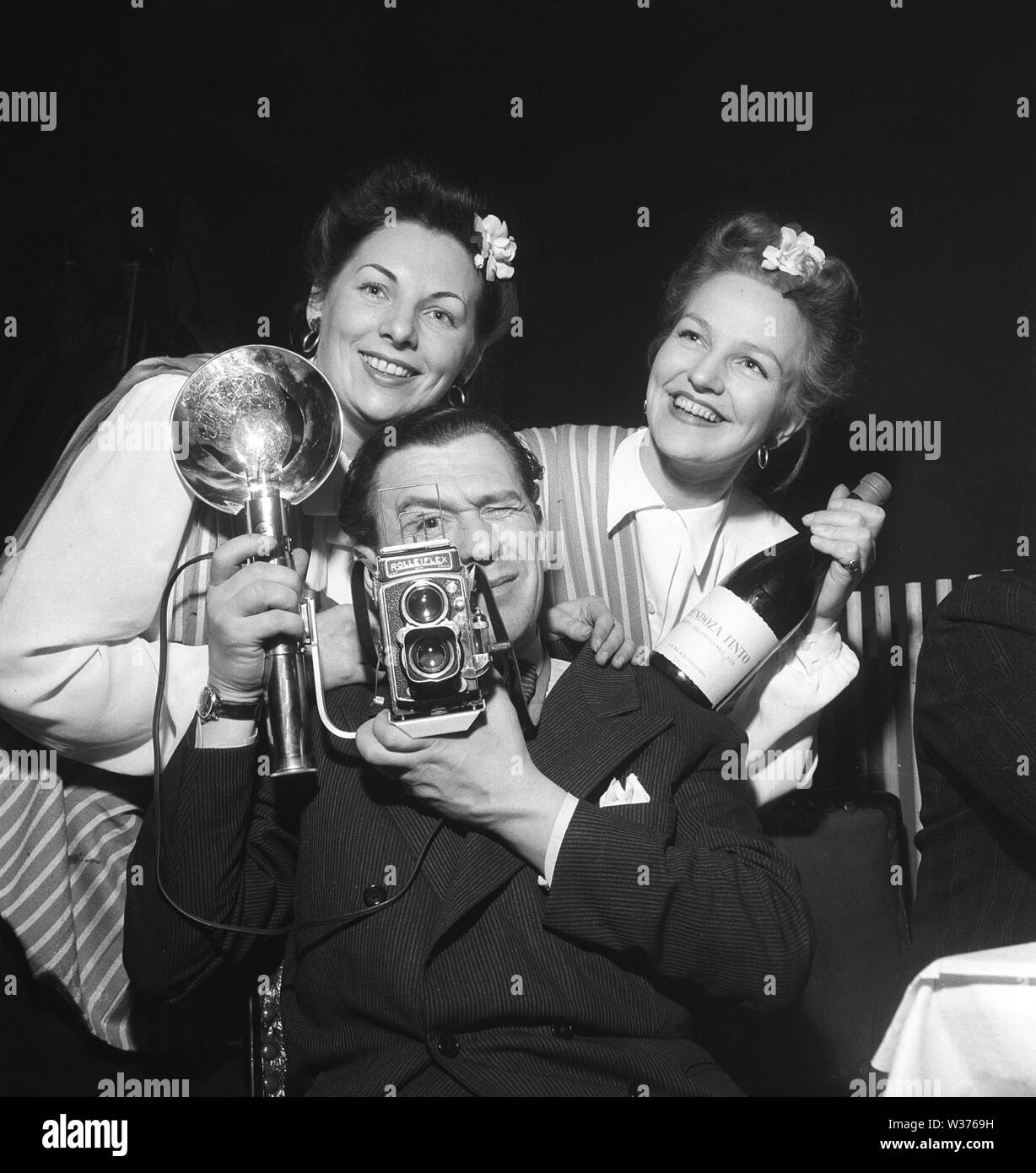 1940s photographer. A man with a Rolleiflex camera and flash aims at something with two girls haning on his shoulders. The Rolleiflex camera for 60 mm film rolls became very popular among professional photographers.   Sweden 1946. Kristoffersson Ref T72-3 Stock Photo