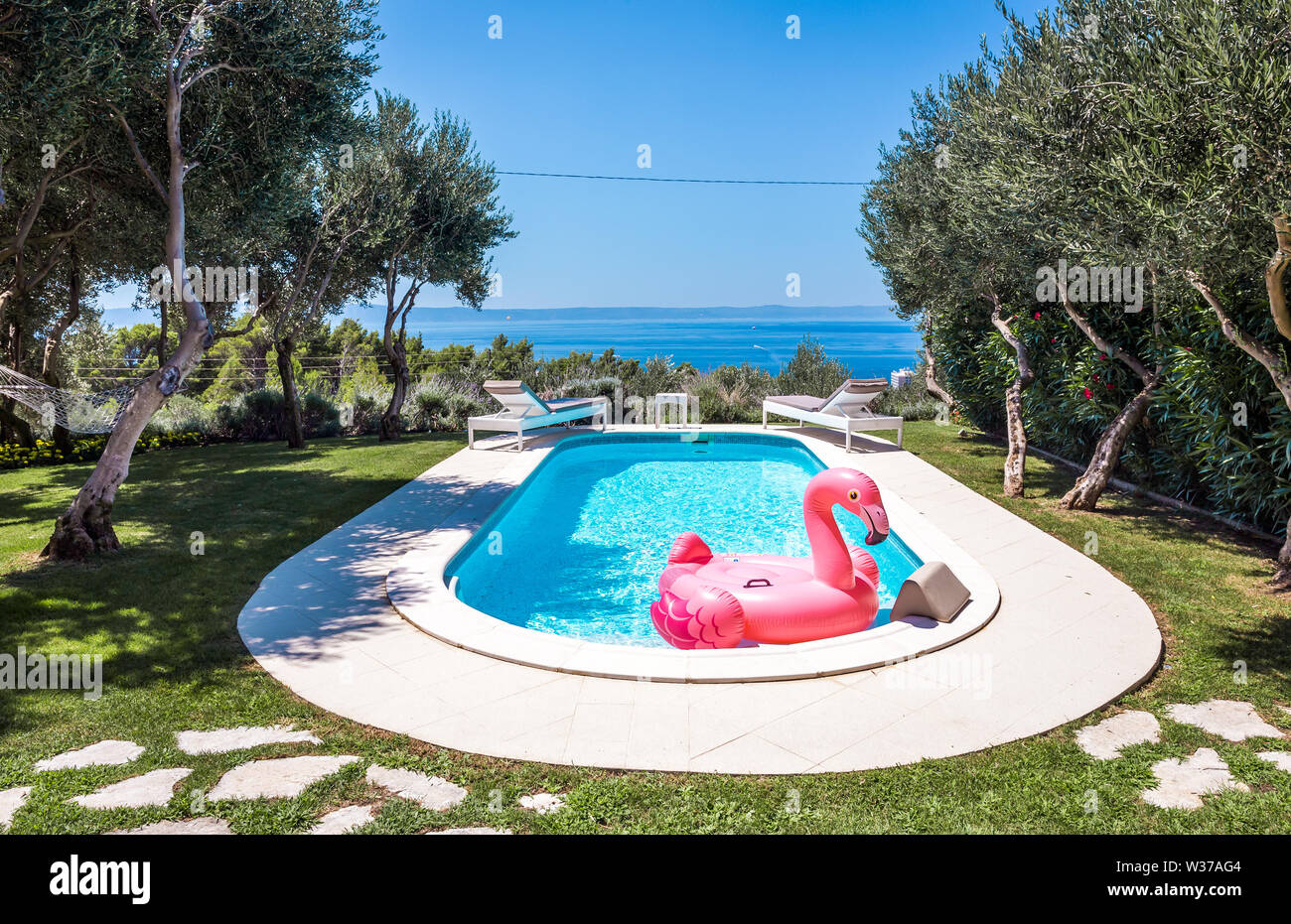 Pink flamingo waterbed in swimming pool with mediterranean sea in the background Stock Photo