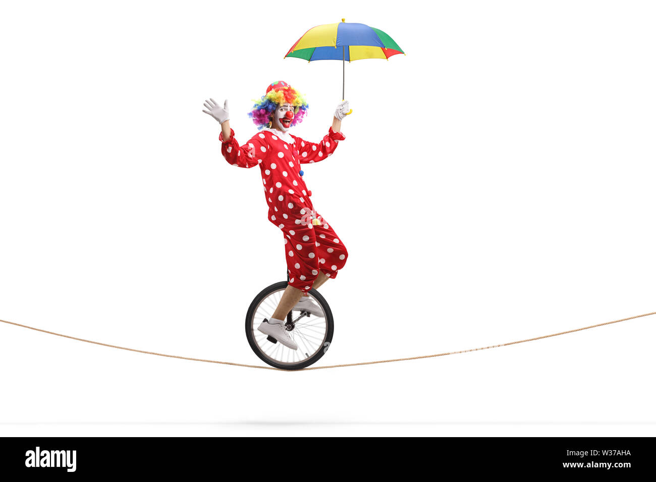 Full length profile shot of a clown riding a unicycle on a rope and holding an umbrella isolated on white background Stock Photo