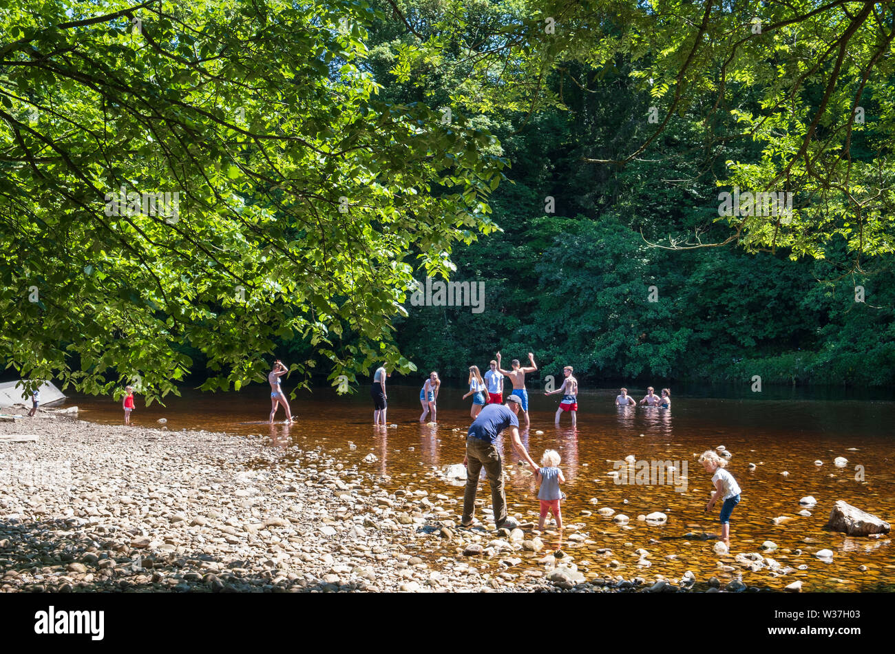 In summer sunshine children, teenagers and families paddling in the River Swale in Richmond North Yorkshire Stock Photo