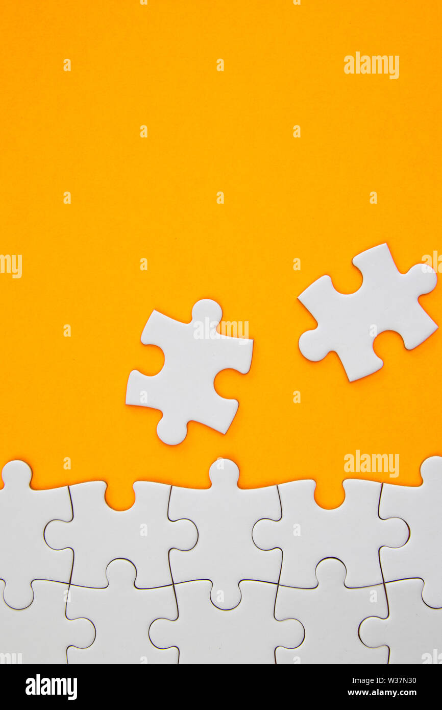 White jigsaw puzzle pieces on orange background with negative space Stock Photo
