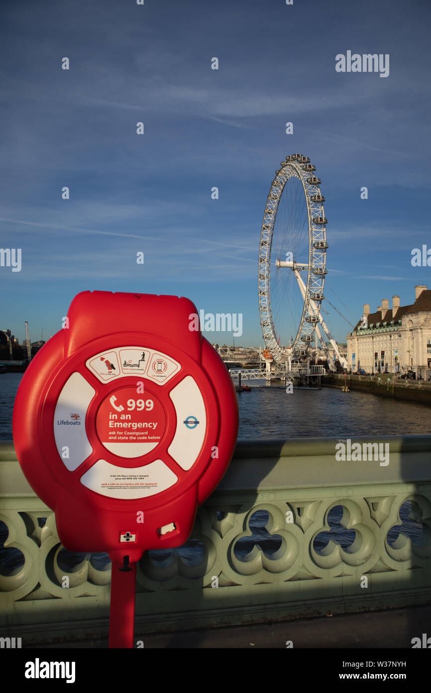 Red Life ring on Westminster Bridge and instructions what to do in case of river emergency, with view of River Thames and the London Eye, London UK Stock Photo