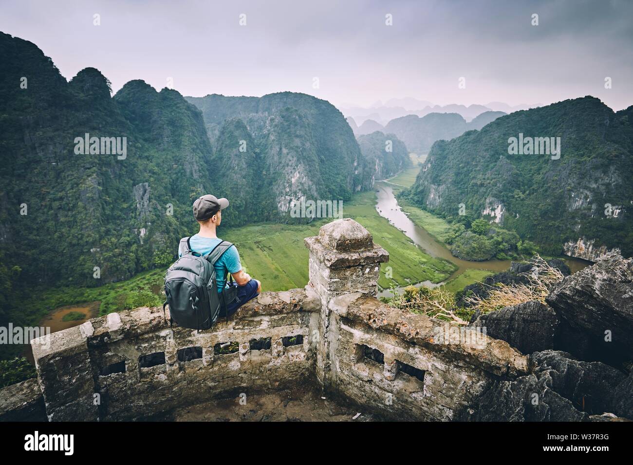 Traveler in Vietnam. Pensive Young man with backpack sitting on peak Mua Cave. Ninh Binh province, Vietnam. Stock Photo