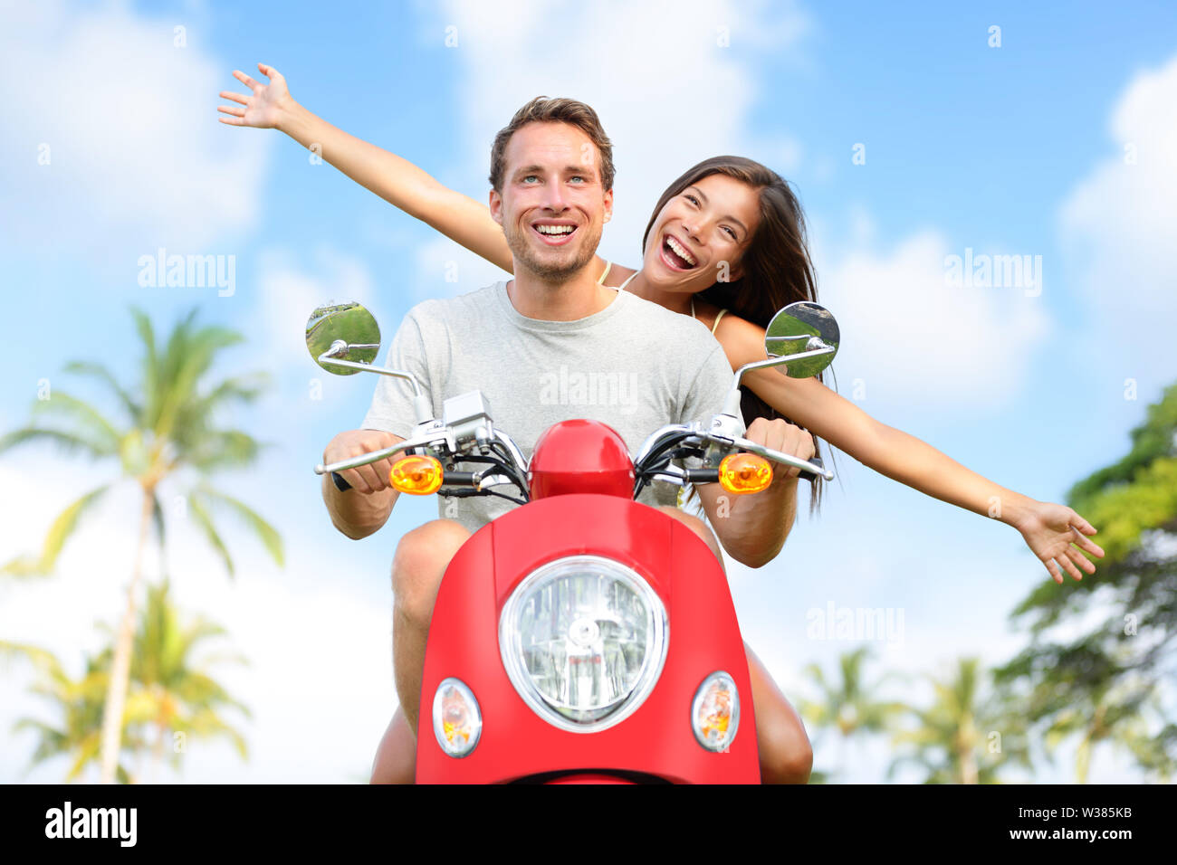 Happy free freedom couple driving scooter excited on summer holidays vacation. Young multiethnic couple in love, Asian woman, Caucasian man Stock Photo