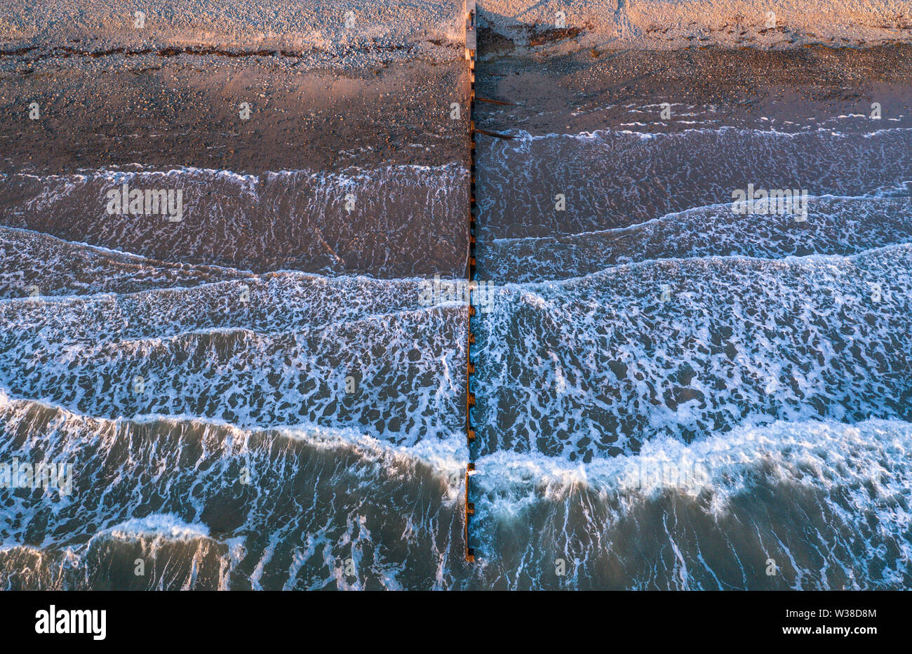 Aerial view over breaking waves on stony shore with wooden breakwater in Barmouth, North Wales, UK Stock Photo
