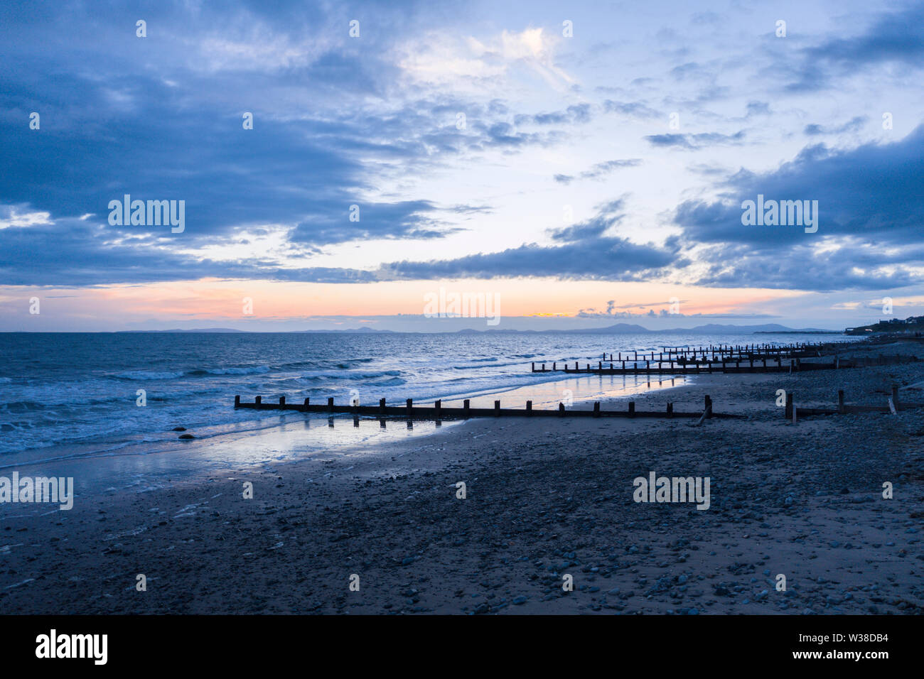 Stormy clouds at twilight over scenic beach with wooden waterbreak. Barmouth in Wales, UK Stock Photo