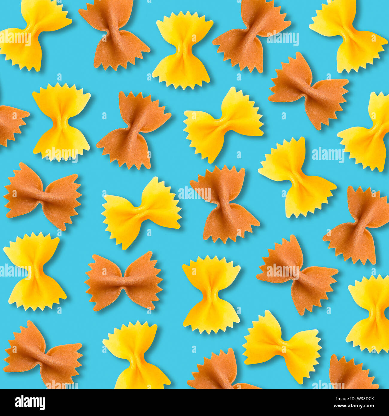 Yellow and brown farfalle pasta pattern on vibrant turquoise color background. Minimal flat lay geometric macaroni food texture Stock Photo