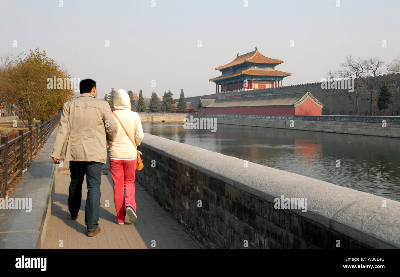 Two people walking by the moat outside the Forbidden City. The Forbidden City has traditional Chinese buildings. The Forbidden City is a UNESCO site. Stock Photo