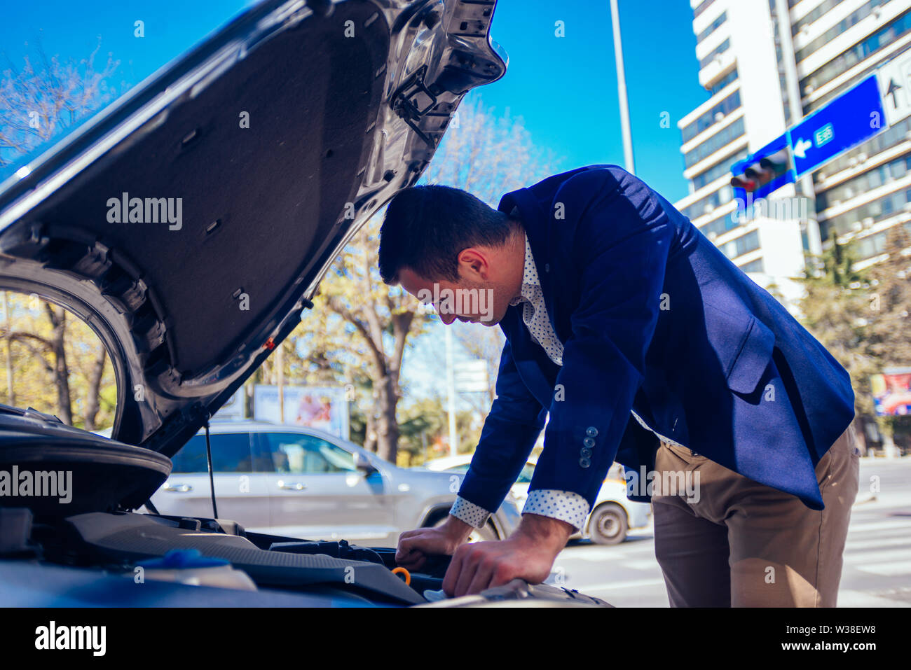 A handsome businessman wearing blue blazer lifting up the hood of his car  and checking the oil level on a sunny day parked on a busy city boulevard  Stock Photo - Alamy