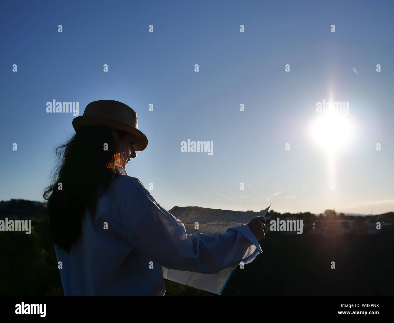 A brunette girl in a hat is considering a terrain map against the rising sun Stock Photo