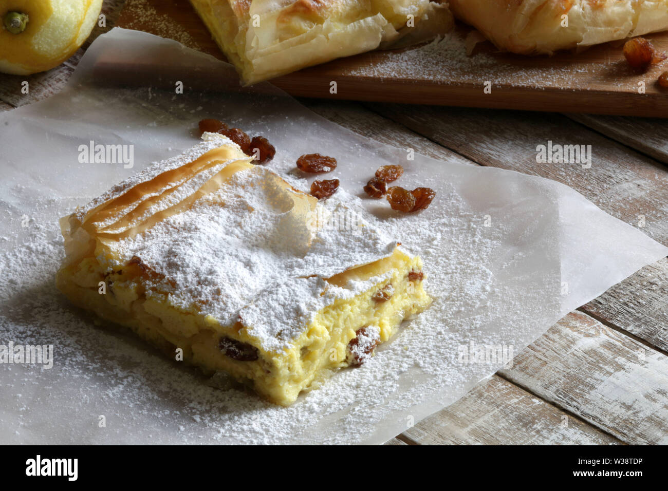 Traditional greek cuisine. Bougatsa, phyllo pastry filled with cream and sultanas, garnished with powdered sugar on wooden table. Stock Photo