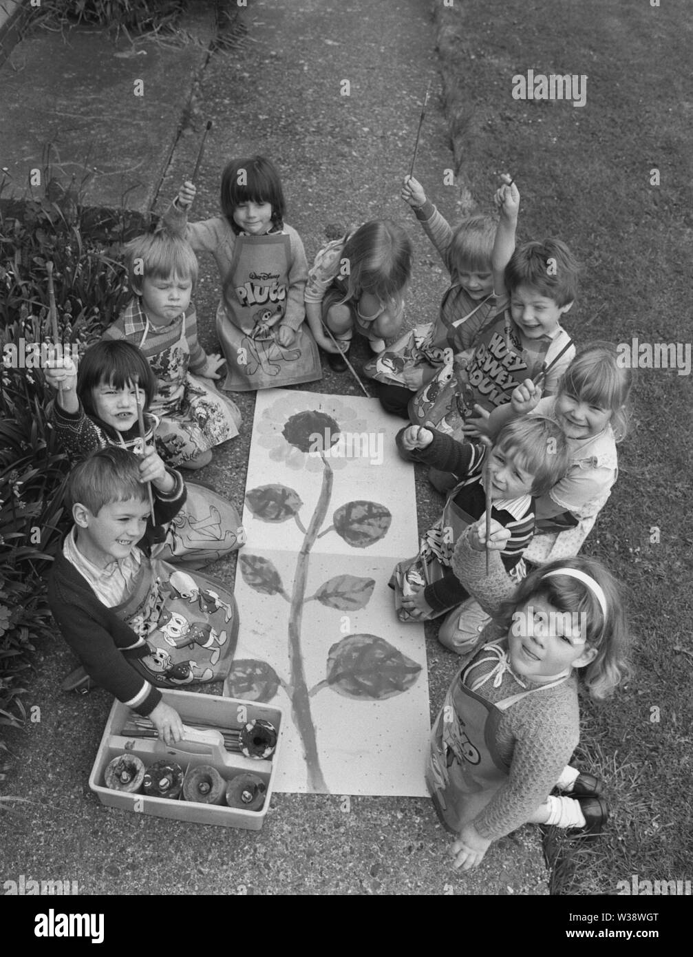 1980s, historical, group of playschool children sitting outside holding up their paint brushes, proud of their painting of a large plant on the ground, England, UK. Stock Photo