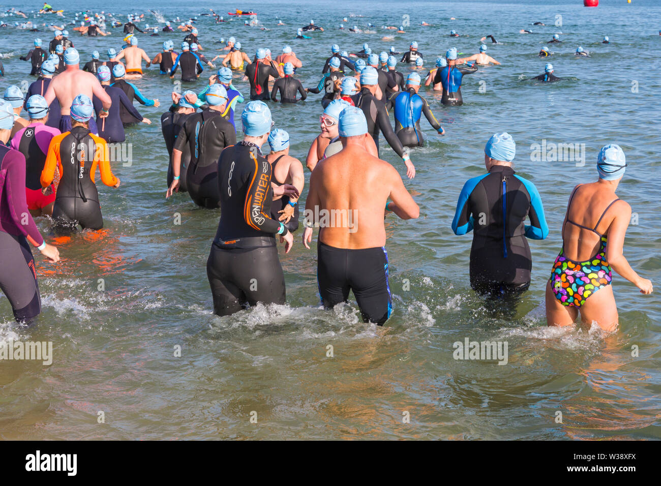 Bournemouth, Dorset UK. 13th July 2019. Pier to Pier sunset swim where swimmers brave the English Channel swimming from Bournemouth to Boscombe piers in 1.4 mile open water challenge, raising funds for BHF, British Heart Foundation. The inaugural sunset swim at Bournemouth where swimmers have 2 hours to complete the swim then relax on the beach to enjoy the sunset, ahead of two more Pier to Pier swims taking place tomorrow during the day – thousands take part in the three swims. A lovely warm sunny evening for the swim. Credit: Carolyn Jenkins/Alamy Live News Stock Photo