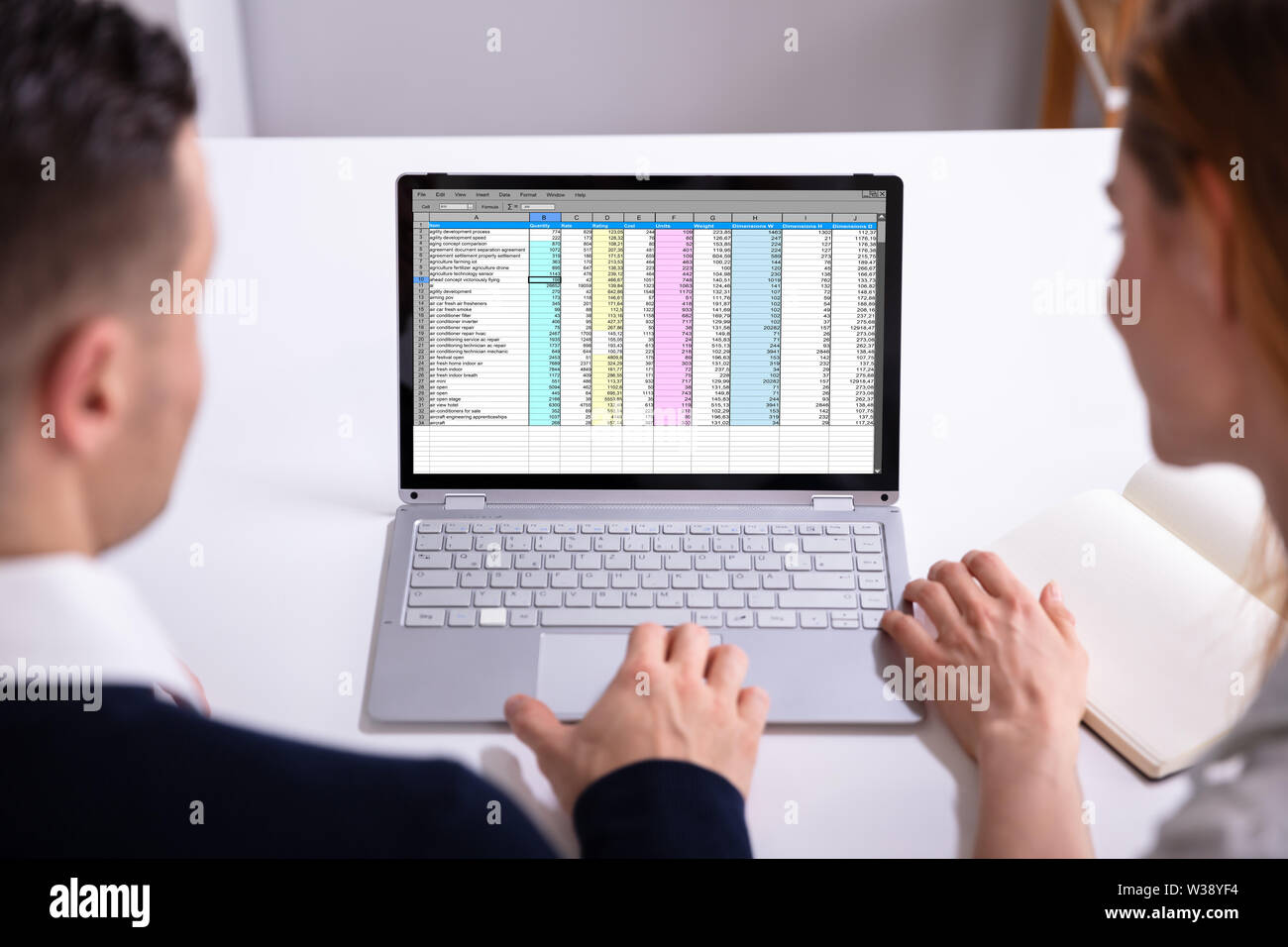 Male And Female Businesspeople Checking Spreadsheet On Laptop Screen Over Desk Stock Photo