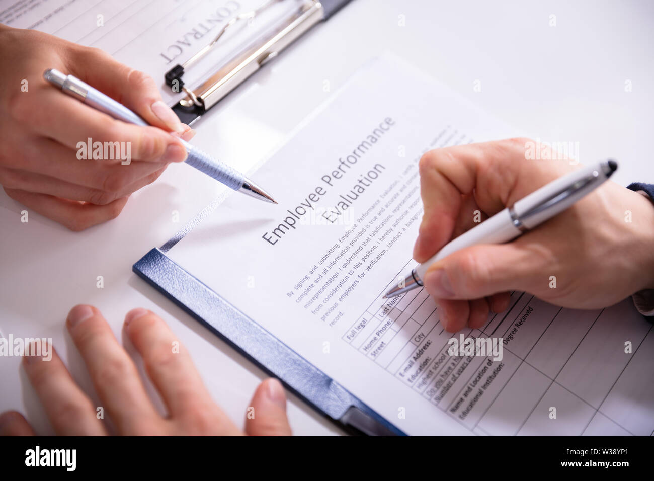 Close-up Of A Person Filling Performance Evaluation Form Of Employee Over Desk Stock Photo