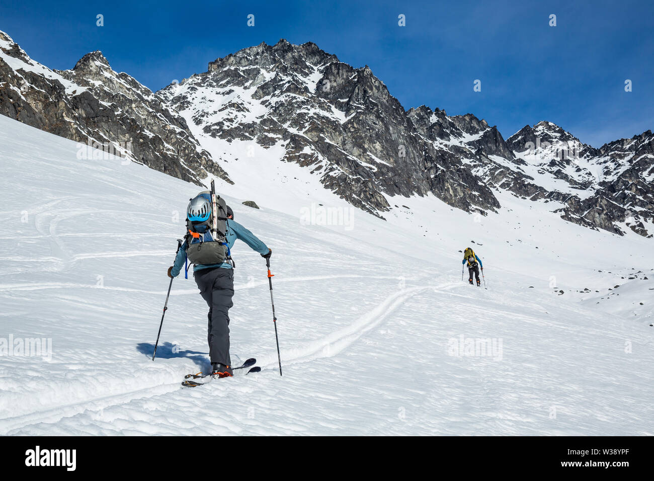 Two skiers skinning uphill on a slope near the old Snowbird Mine site. They are in the Hatcher Pass area of the Talkeetna Mountains of Alaska. Skiing Stock Photo