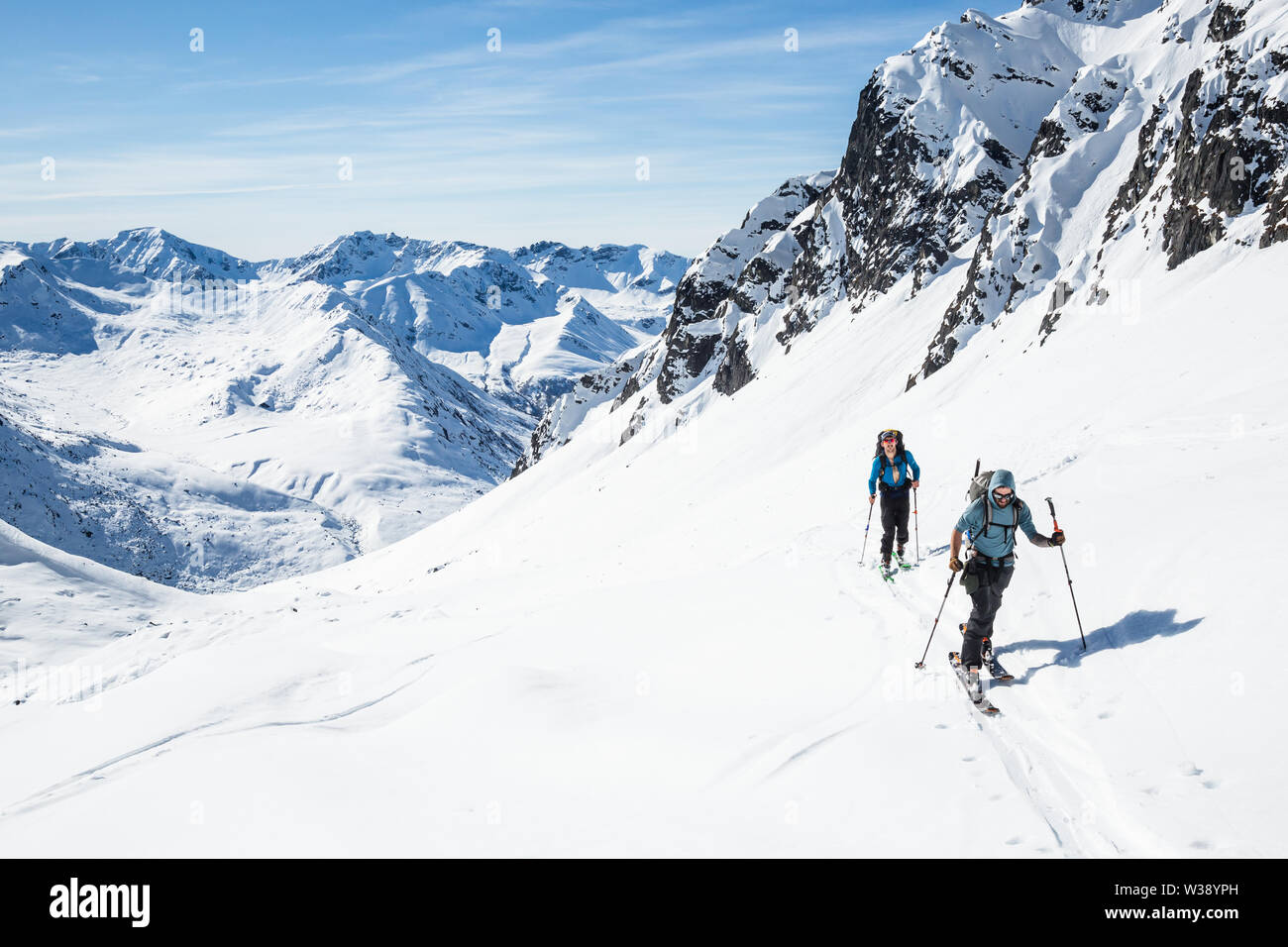 Two skiers skinning uphill on a hot sunny day in the Alaska backcountry