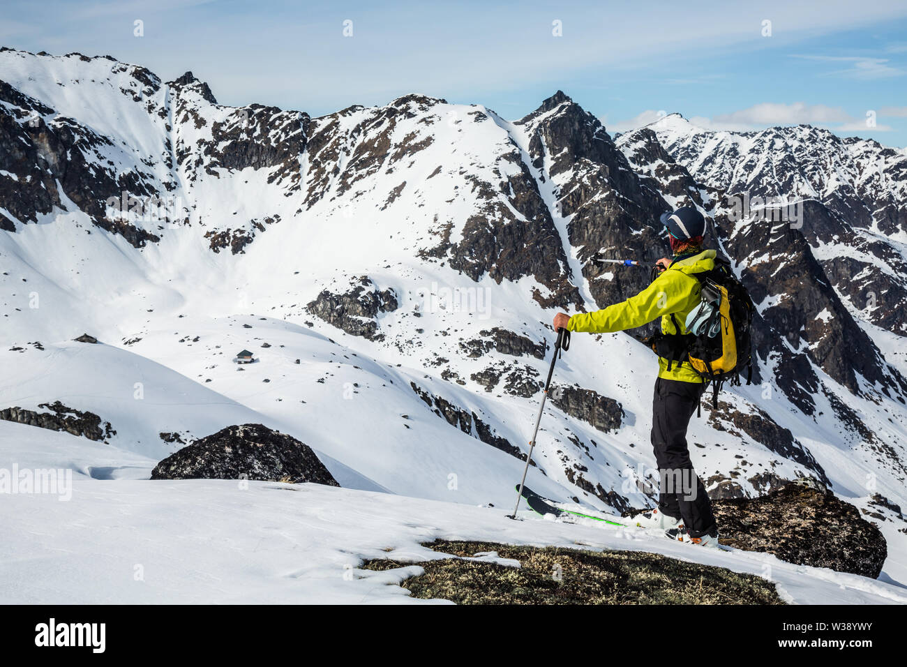 Skier in yellow pointing his pole toward a distant couloir, chute, on a remote peak in the backcountry of the Talkeetna Mountains in Alaska. Stock Photo