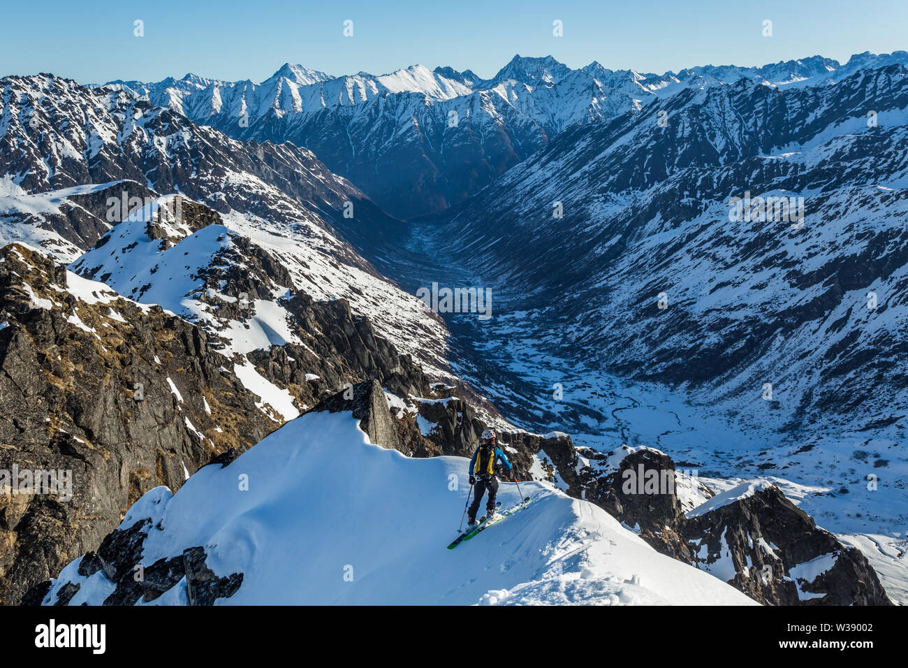 skier stopping on a thin traverse of a small peak over the Bartholf Creek drainage in the Talkeetna Mountains of remote Alaska. Stock Photo