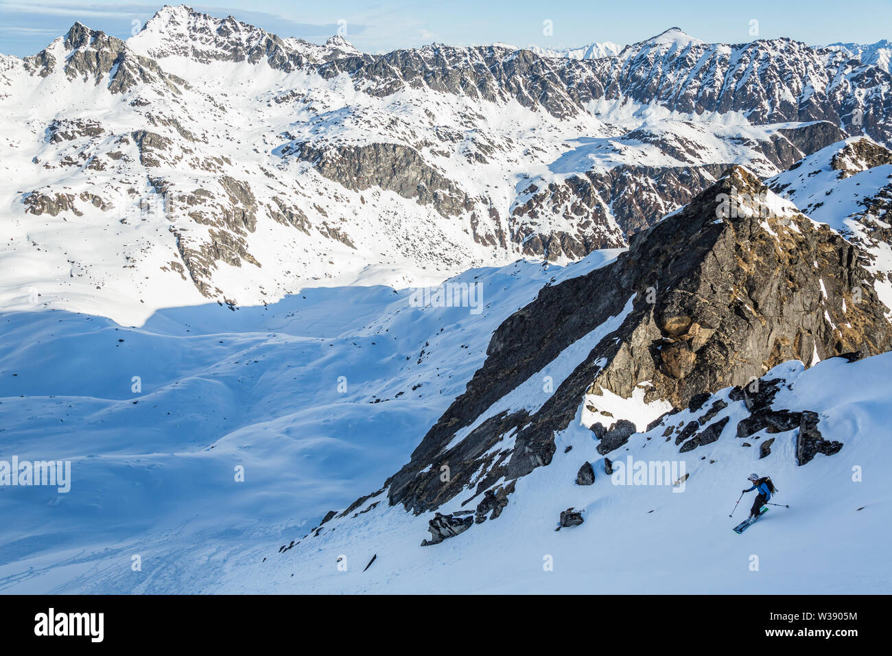 A skier drops into a steep  run on unknown terrain as he traverses mountains and valleys in the Talkeetna Mountains of remote Alaska. Stock Photo