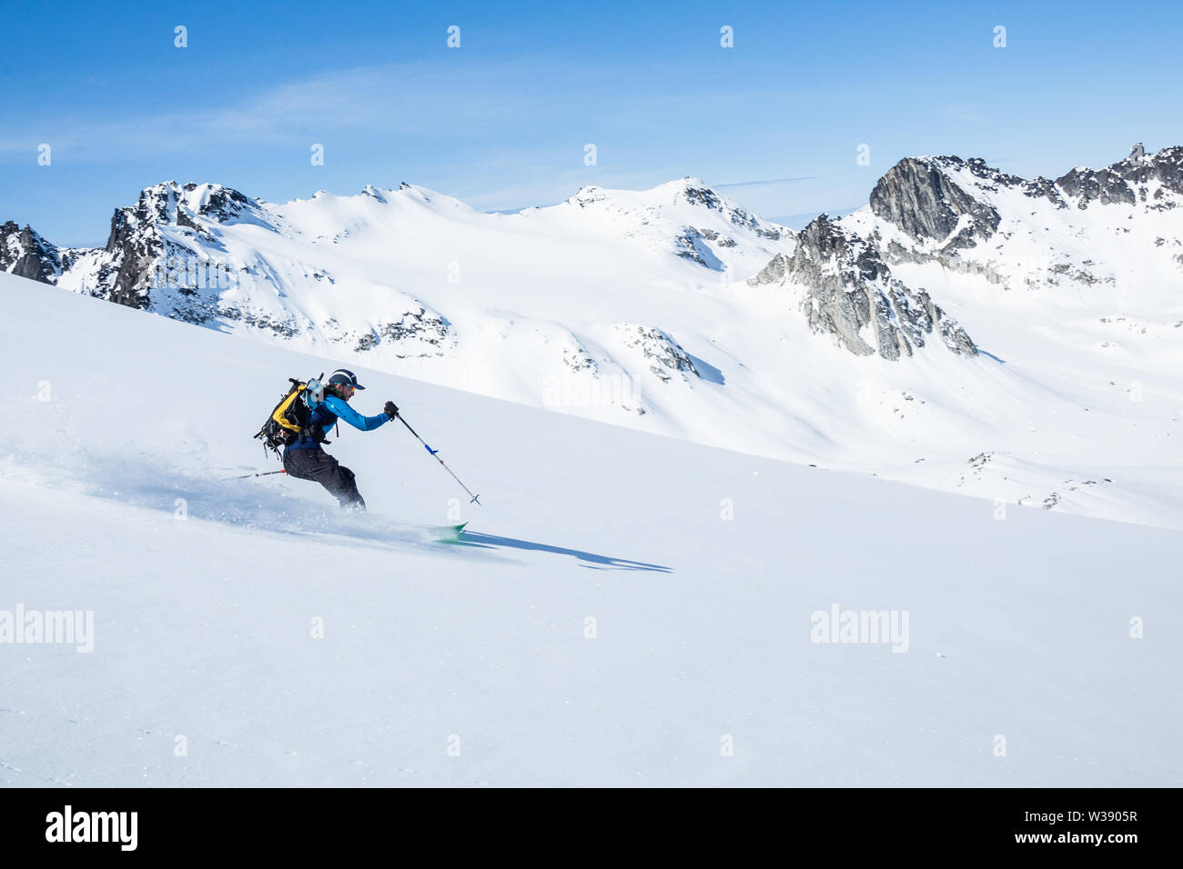 Skier on sunny day and fresh snow ripping down the slope above the Snowbird Glacier in Hatcher Pass, Alaska. Stock Photo