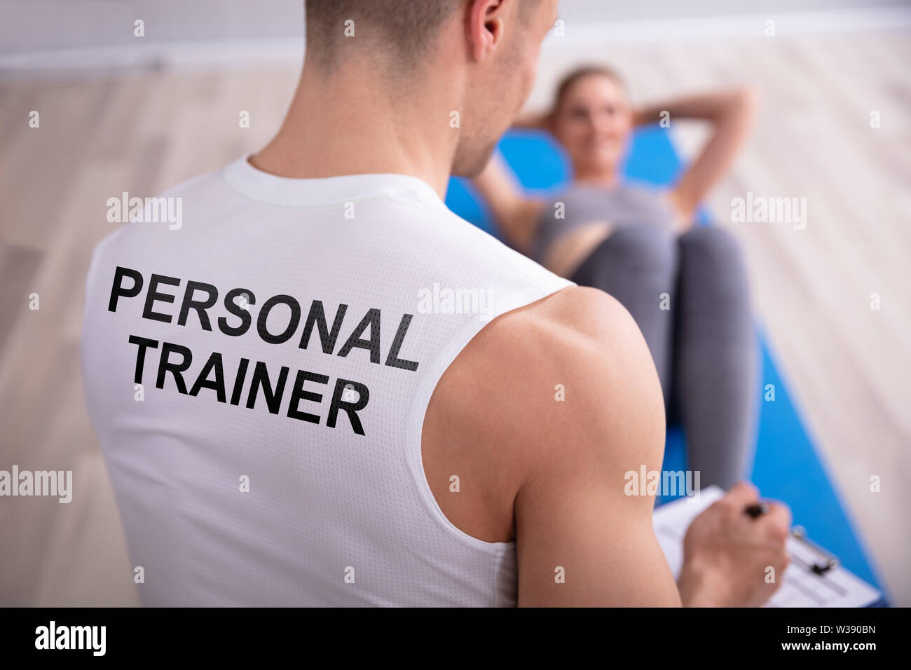 Personal Trainer Looking At Young Woman Doing Exercise On Yoga Mat Stock Photo
