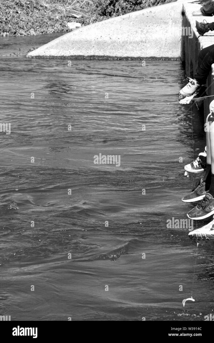 feet tennis shoes hanging over ledge at rivers edge water flowing small fishing line Stock Photo
