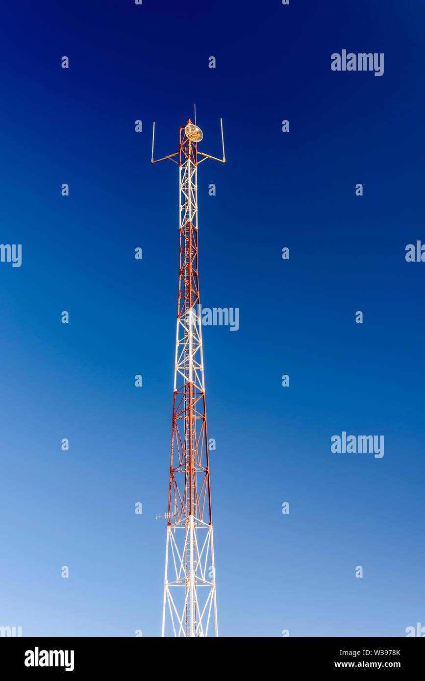 Red and white mobile phone cell tower repeater, with a small microwave dish. Stock Photo