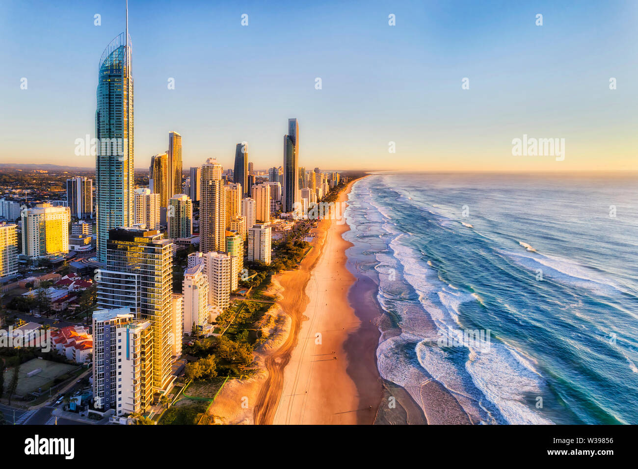 Waterfront behind sandy beach of SUrfers paradise greeting rising sun over Pacific ocean. Aerial view along Gold Coast and line of high-rise towers. Stock Photo